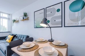 A modern living room with a sofa, a table set with bowls and placemats, wall-mounted shelves with plants, and abstract art. - Perfect for Contractors/Long Stays/Close Amenities (Cheshire West and Chester)