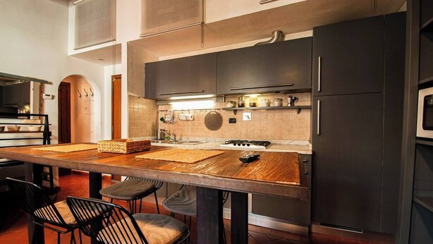 A modern kitchen with dark cabinets, a wooden island, and a gas stove. - Apartmens in Florence Via Porte Nuove (Firenze)