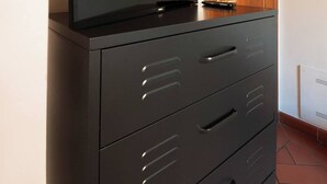 A black filing cabinet with a television on top, a wooden door, and a tiled floor. - Apartmens in Florence Via Porte Nuove (Firenze)