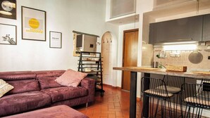 A cozy living room with a large purple sofa, a dining area with a table and chairs, and a kitchen with a large window. - Apartmens in Florence Via Porte Nuove (Firenze)