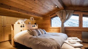 A cozy wooden cabin bedroom with a large bed, a window with a view of a snowy landscape, and a wooden headboard.