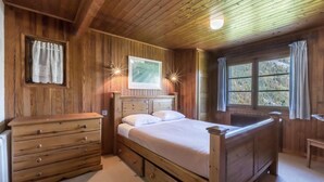 Une chambre à coucher en bois, avec un lit, une commode et une fenêtre avec des rideaux.