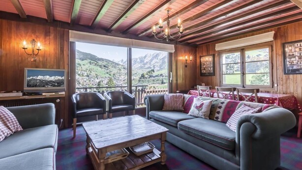 Une pièce chaleureuse avec un plafond en bois, une grande fenêtre donnant sur les montagnes, une télévision et un coin repas avec une table et des chaises.
