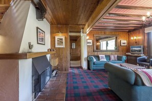 Ein gemütliches Zimmer mit Kamin, einer Couch, einem Fernseher und einem karierten Boden.