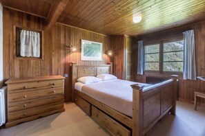 A wooden bedroom with a bed, dresser, and a window with curtains.
