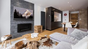 A modern living room with a fireplace, a mounted TV, a dining area, and a kitchen with a wooden door. - Ground floor, balcony, fireplace or stove, tv, 52m², La Clusaz (La Clusaz)