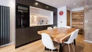 A modern kitchen with a built-in oven, a dining area with a wooden table and white chairs, and a wooden wall panel. - Ground floor, balcony, fireplace or stove, tv, 52m², La Clusaz (La Clusaz)