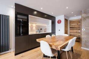 Eine moderne Küche mit Backofen, ein Essbereich mit Holztisch und weißen Stühlen sowie eine Holzwandverkleidung.
