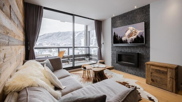 A modern living room with a large window, a grey sofa, a wooden coffee table, and a flat-screen TV mounted on a stone wall. - Ground floor, balcony, fireplace or stove, tv, 52m², La Clusaz (La Clusaz)