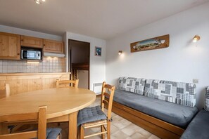 A compact kitchen with wooden cabinets, a microwave, and a dining area with a round table and chairs.