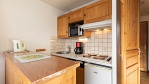 A compact kitchen with wooden cabinets, a microwave, a coffee maker, and a small refrigerator.