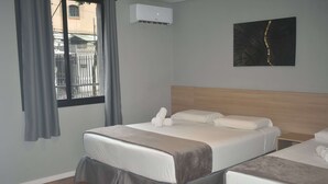 A hotel room with two beds, a grey wall, a window with curtains, an air conditioning unit, and a painting on the wall. - Unity Hotel Campinas (Campinas)