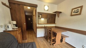 A compact room with a wooden dining table, a small kitchenette, a gray sofa, and a wooden wardrobe. - 100m from ski slopes, 1st floor, balcony, 21m², Tignes (Tignes)