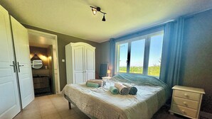 A bedroom with a bed, a nightstand, a wardrobe, and a window with a view. - Spacious cottage with air conditioning, wood fire & panoramic views - pool shared (Paulhiac)