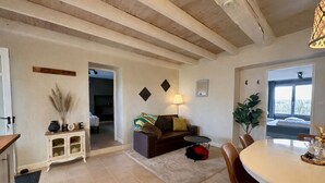 A living room with a sofa, a dining table, and a kitchen area with cabinets. - Spacious cottage with air conditioning, wood fire & panoramic views - pool shared (Paulhiac)