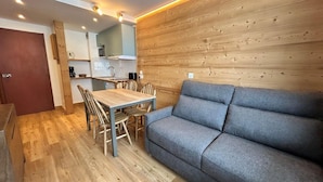 A modern kitchen with wooden paneling, a dining area with a wooden table and chairs, and a grey sofa. - 100m from ski slopes, 1st floor, balcony, 22m², Tignes (Tignes)