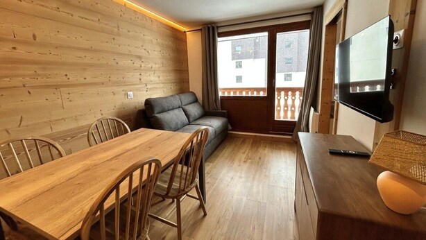 A cozy room with a wooden dining table, chairs, a sofa, and a TV on a wooden stand. - 100m from ski slopes, 1st floor, balcony, 22m², Tignes (Tignes)
