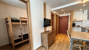 Una stanza compatta con un letto a castello, una piccola cassettiera in legno, una televisione e un angolo cottura.