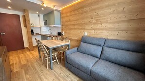 Una cucina moderna con pannelli in legno, una zona pranzo con tavolo e sedie in legno, e un divano grigio.