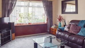 A living room with a glass coffee table, a leather sofa, a TV, and a window with curtains. - 3 bedroom accommodation in Stirling (Stirling)