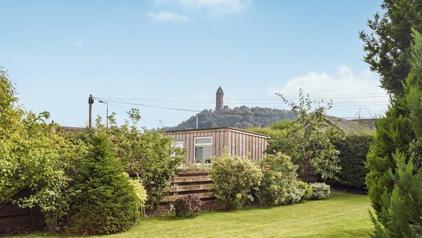 A small wooden building with a door and windows, surrounded by lush greenery and a well-maintained lawn. - 3 bedroom accommodation in Stirling (Stirling)