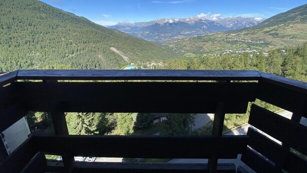Un balcone con vista su un paesaggio montuoso, che include una valle e cime lontane.