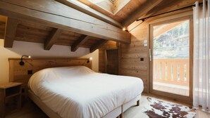 A wooden cabin bedroom with a bed, a nightstand, a skylight, and a balcony with a view. - 1st floor, view mountain, balcony, fireplace or stove, tv, ski locker, 119m², La Clusaz (La Clusaz)