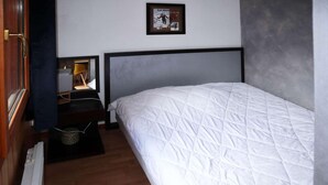 Een slaapkamer met een bed, nachtkastje, lamp en een ingelijst schilderij aan de muur.