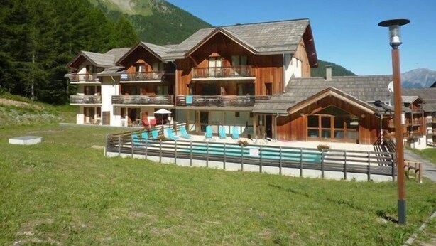 Een chalet met meerdere verdiepingen, houten balkons, een zwembad en een berg op de achtergrond.