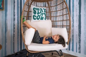 A child lying in a wicker chair with a pillow that says 'STAY COZY.' - 5BR Villa+ Spa & Pool Oasis+GameRoom+Themed Rooms (Davenport)
