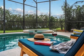 A poolside area with a lounge chair, a book, a straw hat, and a glass of red wine. - 5BR Villa+ Spa & Pool Oasis+GameRoom+Themed Rooms (Davenport)