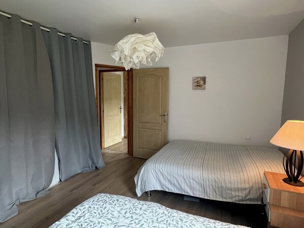 Un dormitorio con dos camas, una puerta de madera, una pequeña decoración en la pared y una lámpara en una mesita de noche.