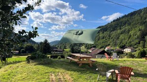 A picnic setup with a table and chairs in a grassy field, surrounded by houses and a forested hill in the background. - 5-person apartment with outdoor area (Saint-Maurice-sur-Moselle)