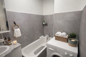 A modern bathroom with a bathtub, a washing machine, a sink, and a towel rack. - Horizon Bleu with terrace in Sainte-Maxime (Sainte-Maxime)