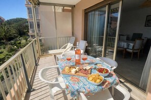 Ein Balkon mit Tisch, gedeckt für eine Mahlzeit, darunter eine Weinflasche, Käse und Snacks.