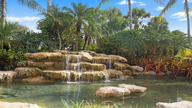 A natural water feature with cascading water over rocks, surrounded by tropical vegetation. - Fantastic 2-bedroom 2 bath condo for Seasonal Rent in Tequesta Fla (Tequesta)