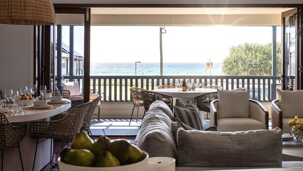 Uma sala de jantar com vista para o mar, mobiliário de vime e uma mesa posta para refeição.