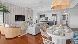 Uma sala de estar moderna com sofá, cadeiras, uma mesa de jantar posta para seis pessoas e uma cozinha ao fundo.