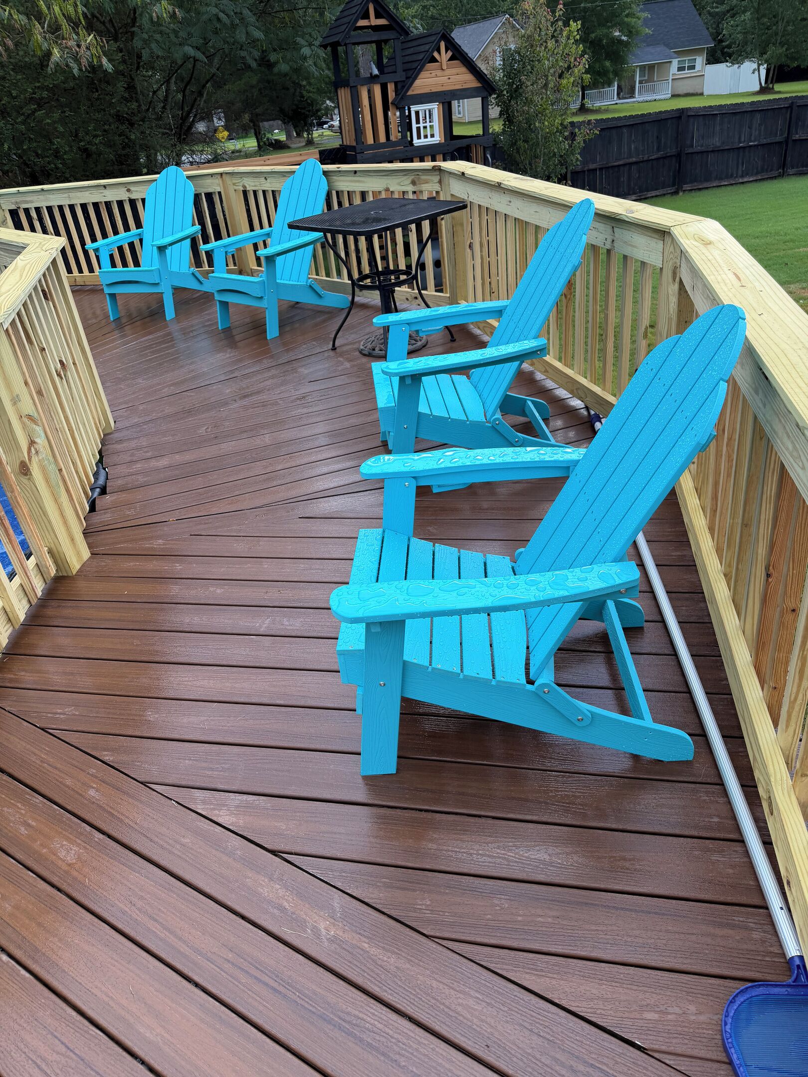 A wooden deck with blue Adirondack chairs and a small table.