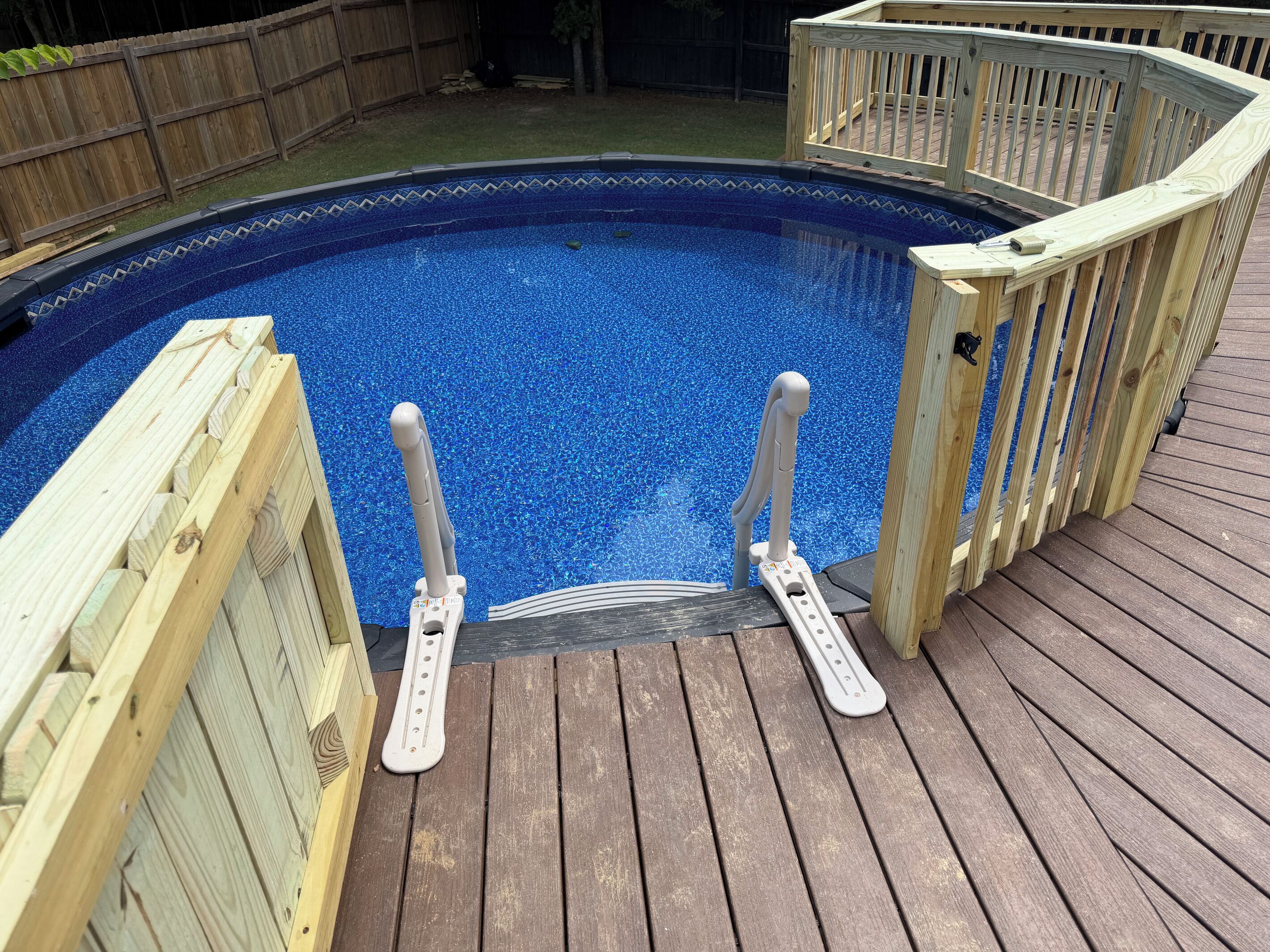 A wooden deck surrounding a swimming pool with a blue mosaic border.