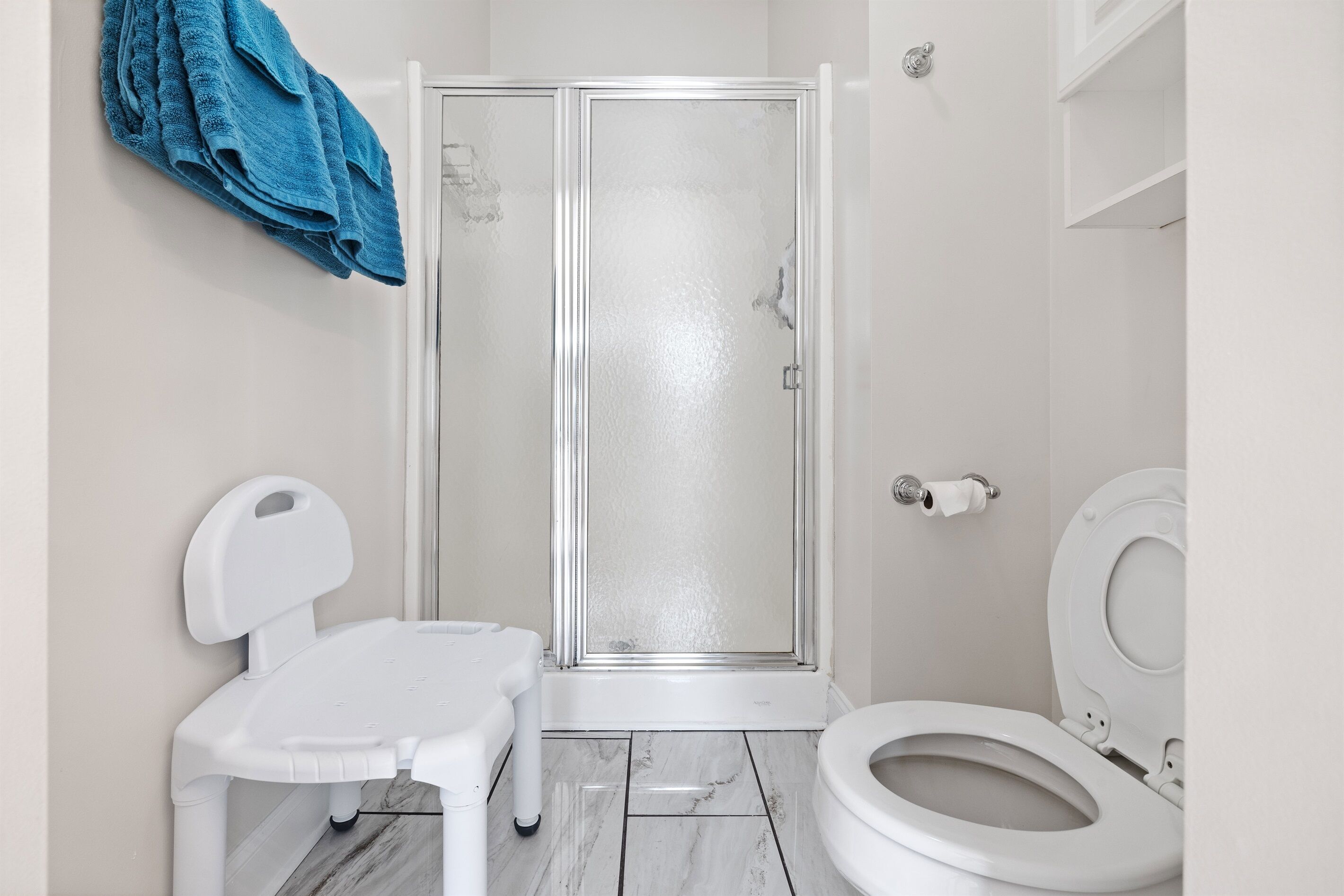 Een badkamer met een wit toilet, een douchecabine en een kleine witte stoel.