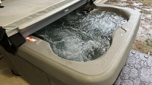 Un jacuzzi dont le couvercle est entrouvert, l’eau éclabousse et une étiquette est fixée sur le bord.