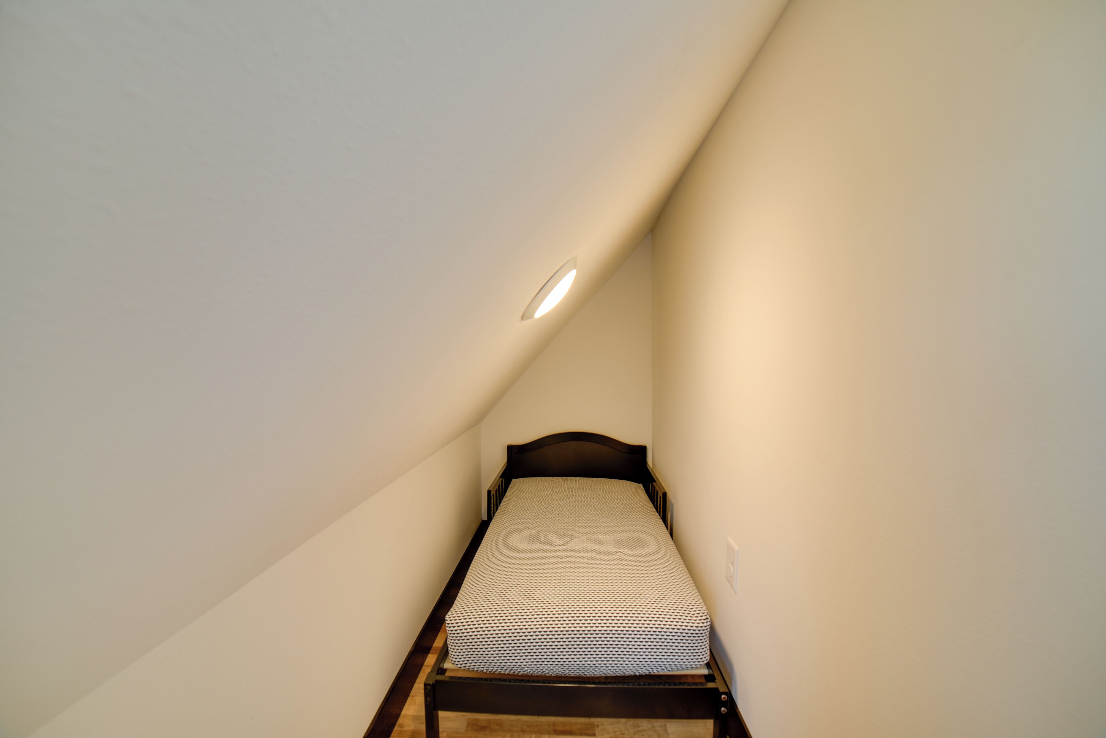 A small, narrow room with a single bed and a sloped ceiling.