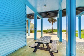 Un espacio al aire libre techado con una mesa de picnic, columnas azules y vistas a la playa.