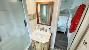 Un baño con ducha de vidrio, lavamanos con tocador de madera y un espejo.
