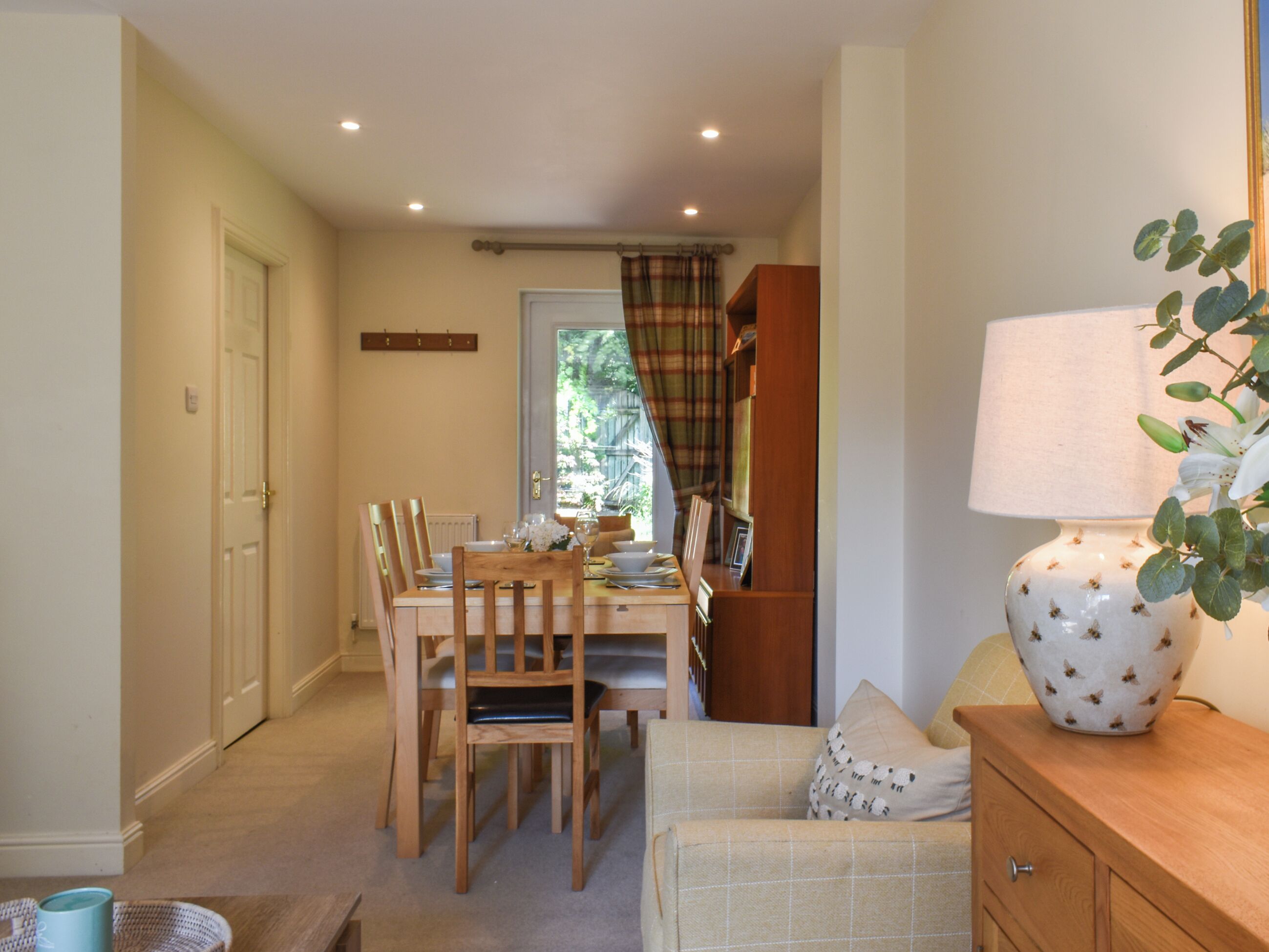 Un coin repas avec une table dressée pour quatre personnes, des chaises en bois, une lampe et une bibliothèque.