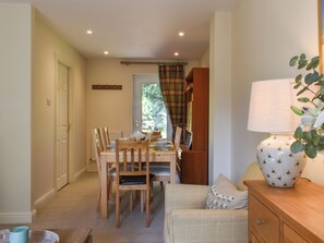 A dining area with a table set for four, wooden chairs, a lamp, and a bookshelf.