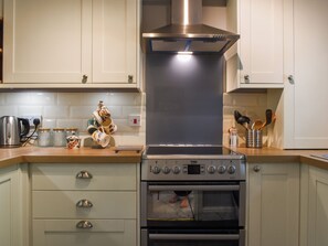 A kitchen with a stainless steel range hood, a built-in oven, and a countertop with a kettle and jars.