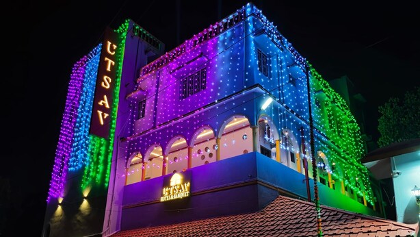 Un hôtel avec une enseigne indiquant « UTSAY HOTEL & BANQUET » et une façade colorée agrémentée de guirlandes lumineuses.