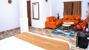 Une chambre d’hôtel avec un lit, un canapé orange, une petite table ronde et un téléviseur.
